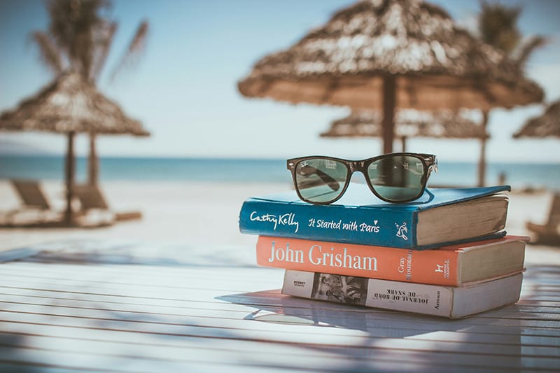 pile of books sitting on table overlooking the beach.
